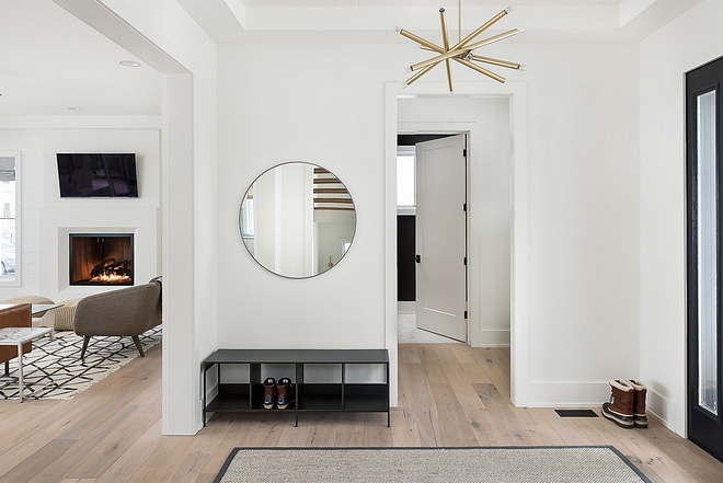 The foyer features White Oak hardwood floors, white walls, modern brass chandelier and a round mirror